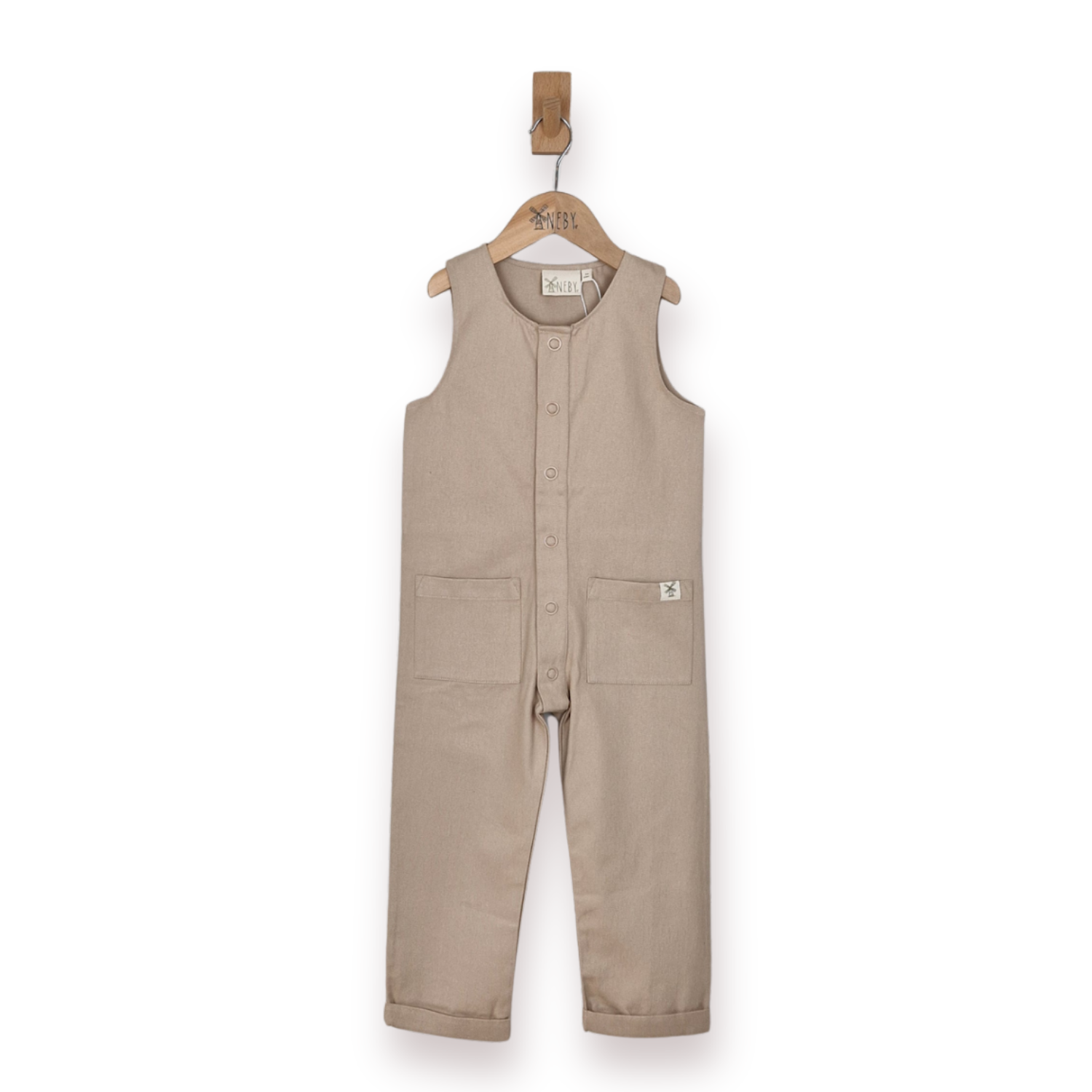 A sleeveless beige children's jumpsuit with a button front and two front patch pockets, hanging on a wooden hanger against a plain white background.