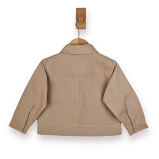 A light tan children's jacket shown from the back, hanging on a wooden hanger with a wooden peg hook above it, against a plain white background.