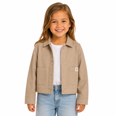 A young girl smiling and wearing a beige shacket over a white t-shirt and blue jeans, photographed against a solid white background.