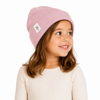 A young girl with brown hair wearing a dusty pink ribbed knit beanie with a small white square patch featuring a green bee logo, set against a plain white background.