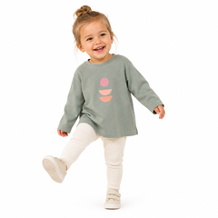 Child wearing a green long-sleeve shirt with a pink abstract design on a white background