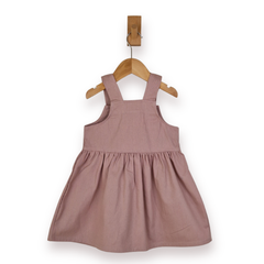 A sleeveless dusty rose pink pinafore dress for a toddler, hanging on a wooden hanger from a wooden peg against a plain white background.