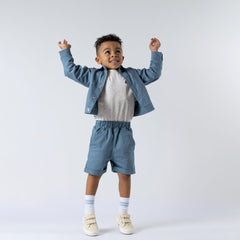 Young boy wearing a blue boxy jacket with matching shorts and speckled t-shirt