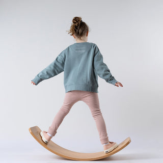 Young girl from behind standing on wobble board whilst modelling blue jumper with sunrise design below the neck