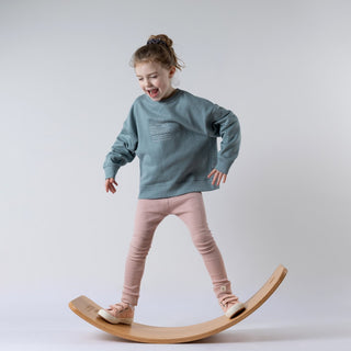 Young girl standing on wobble board whilst modelling blue jumper with subtle sunrise design on the front