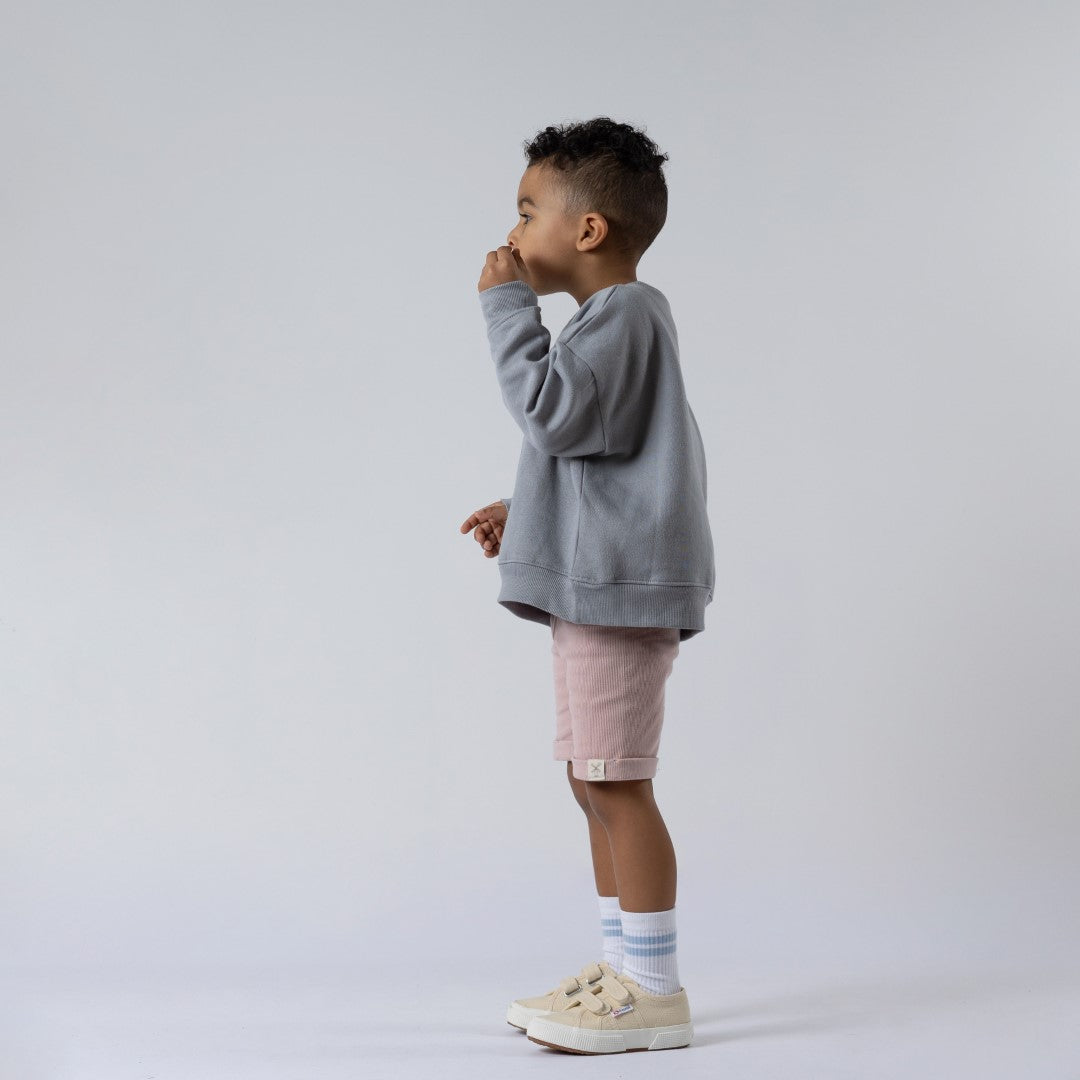 Young boy wearing pink shorts and grey jumper blowing bubbles