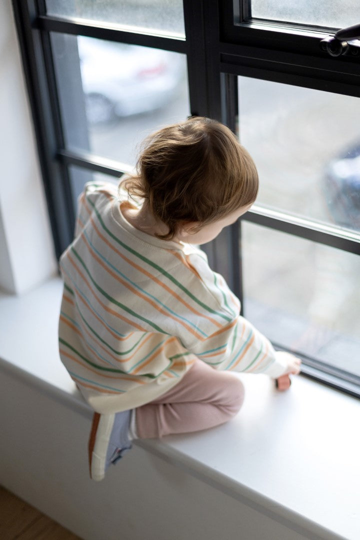 Small model looking out of a window with her back to camera whilst modelling the striped Aneby jumper