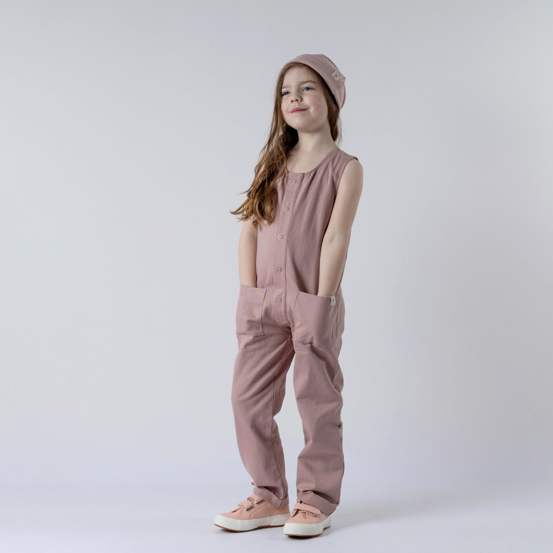 Girl with hands in pocket wearing a sleeveless pink sleepsuit and beanieGirl with hands in pocket wearing a sleeveless pink sleepsuit and beanie
