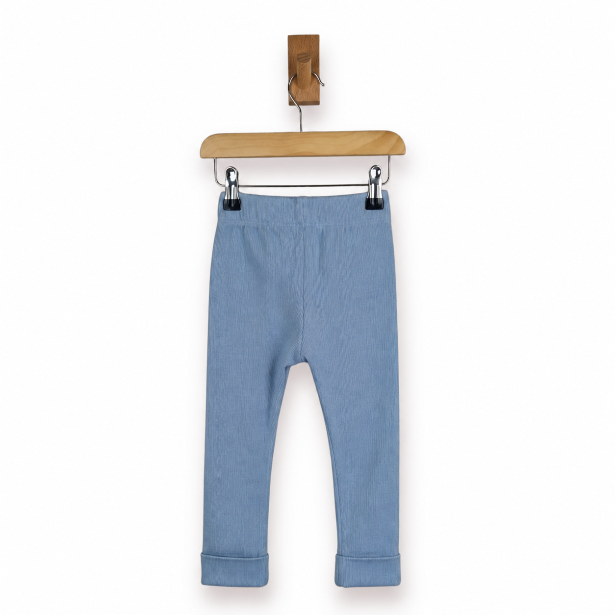 Dusty blue children's leggings with an elastic waistband and rolled cuffs, hanging from a wooden hanger against a plain white background.