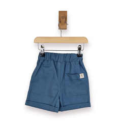 Blue cotton chino shorts with an elastic waistband, rolled hems, and a side pocket, hanging from a wooden hanger on a white background.