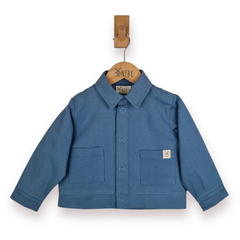 A blue cropped jacket for toddlers, featuring a button-up front, two front patch pockets, and a small woven logo patch on the left pocket, hanging on a wooden hanger with a wooden peg against a white background.