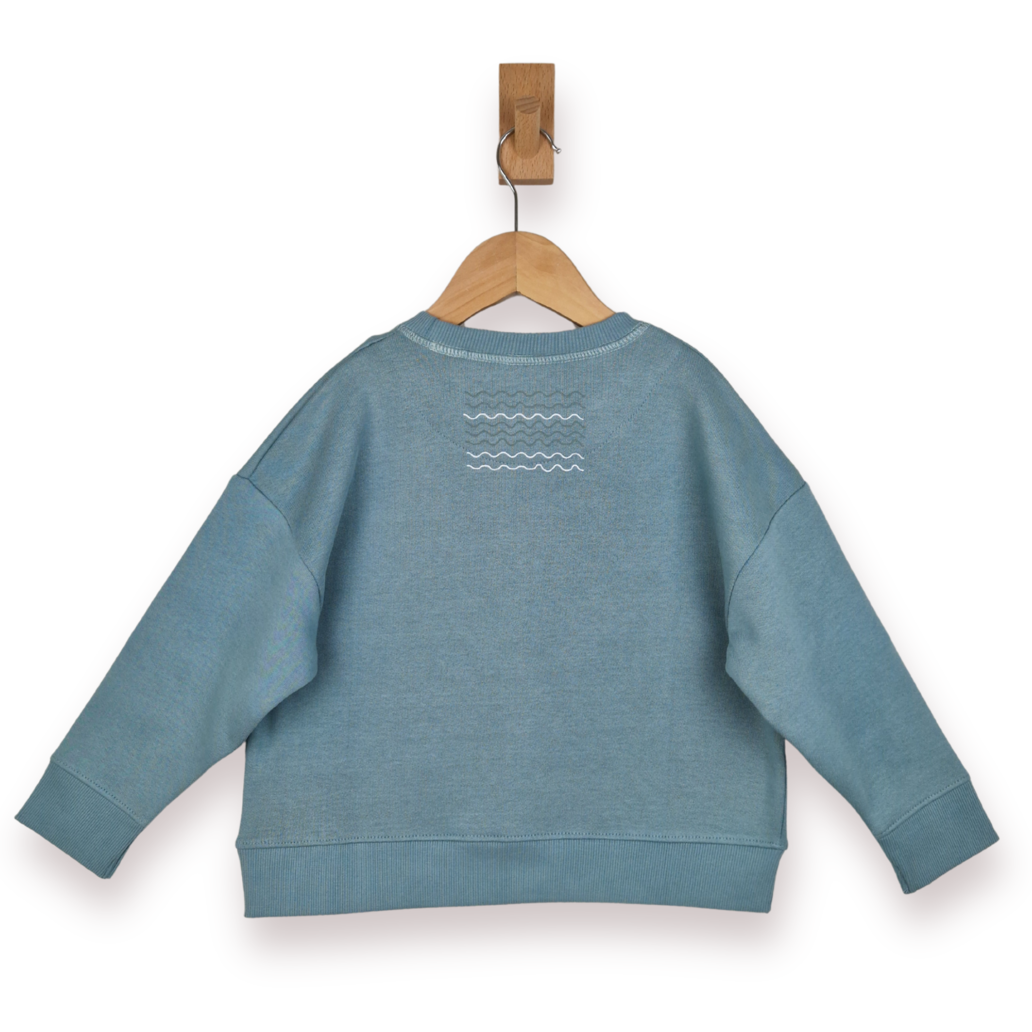 Blue sweatshirt with a wave design on the back, hanging on a wooden clip against a white background.