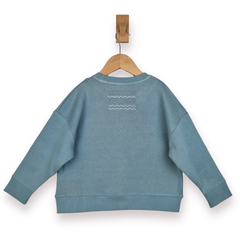 Blue sweatshirt with a wave design on the back, hanging on a wooden clip against a white background.