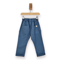 Blue chino trousers with an elastic waistband, two large patch pockets, and rolled cuffs, hanging from a wooden hanger on a white background.