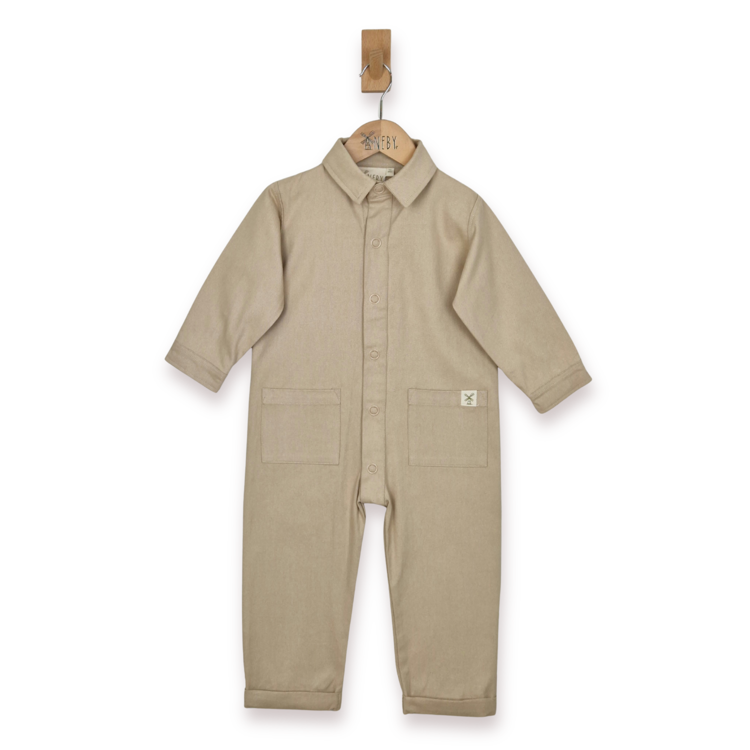 Ecru boilersuit, with collar, poppers and front patch pockets. Image taken against a white background, hanging from a wooden Aneby hanger. 