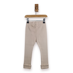 A pair of kids light beige leggings with rolled cuffs, hanging from a wooden hanger with black clips against a plain white background.
