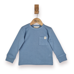 A children's dusty blue long-sleeve crewneck rib top with a chest pocket, hanging on a wooden hanger against a plain white background.