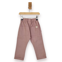 A pair of dusty rose pants hanging from a wooden hanger against a plain white background.