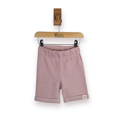A pair of dusty pink ribbed knit shorts for toddlers, hanging from a wooden hanger against a clean white background.