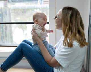 Mum holding baby sitting in front of window smiling at each other