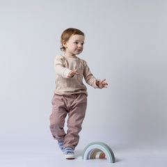 Young girl wearing long sleeve neutral beige top with patch pocket and dusty pink trousers