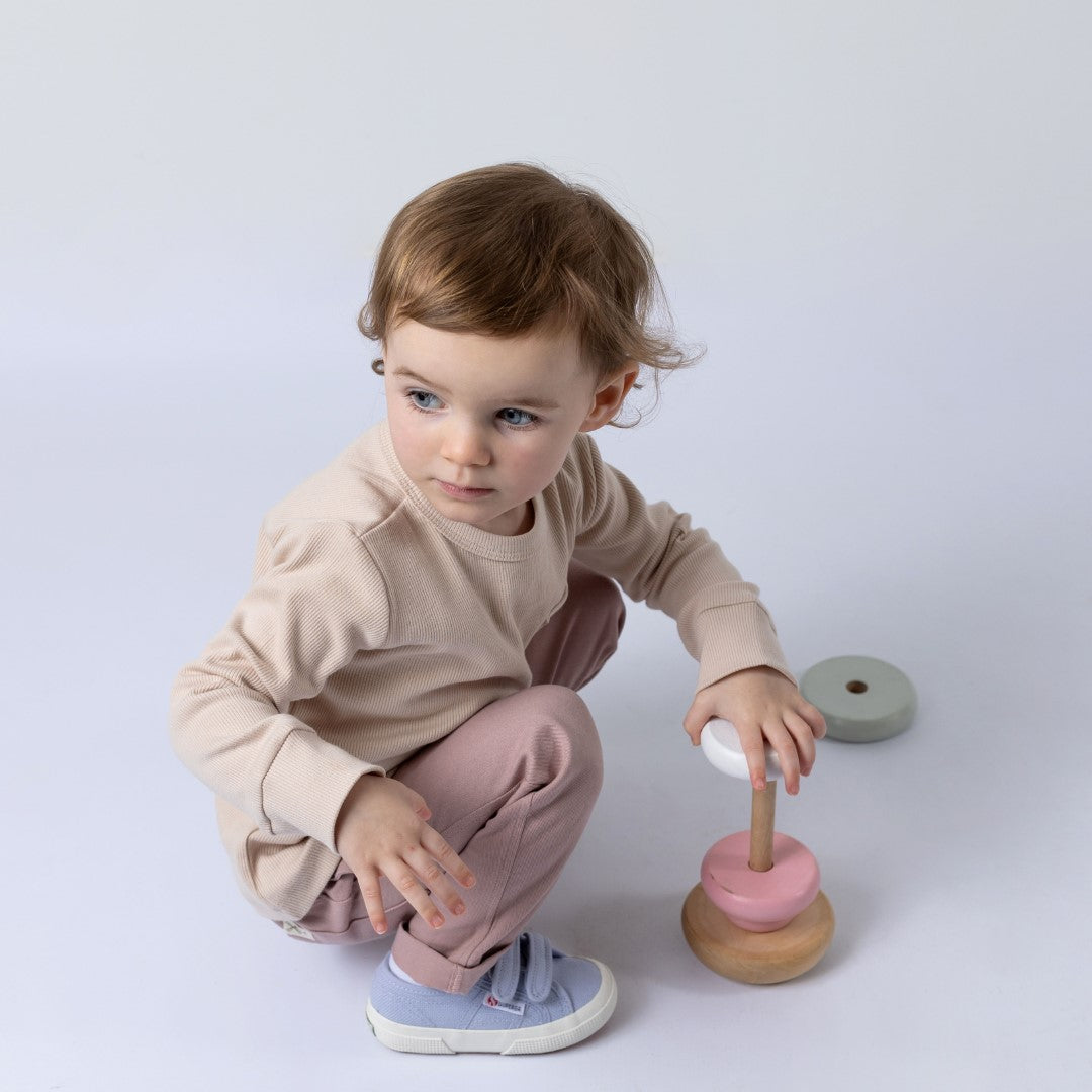 Small girl playing with wooden stacker wearing beige jumper and pink trousers