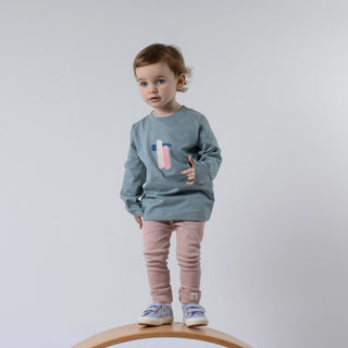 Small girl wearing blue long-sleeved t-shirt with paint stroke effect on the front, standing on wooden wobble board