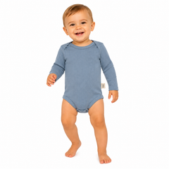A smiling baby wearing a blue long-sleeve ribbed bodysuit, standing barefoot against a solid white background.