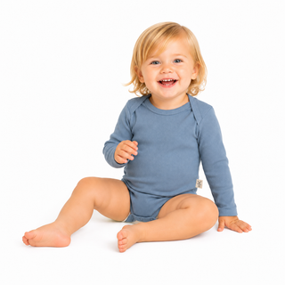 A smiling toddler with blonde hair sits on a white studio background wearing a dusty blue long-sleeve romper.