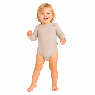 A smiling toddler with blonde hair wearing an oat long-sleeve bodysuit, standing barefoot against a solid white background.