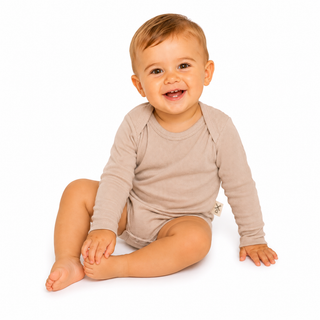 A smiling baby sitting on a white background, wearing a light beige long-sleeve romper.