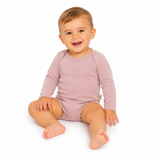 A smiling baby sitting cross-legged on a white background, wearing a dusty pink long-sleeve bodysuit.