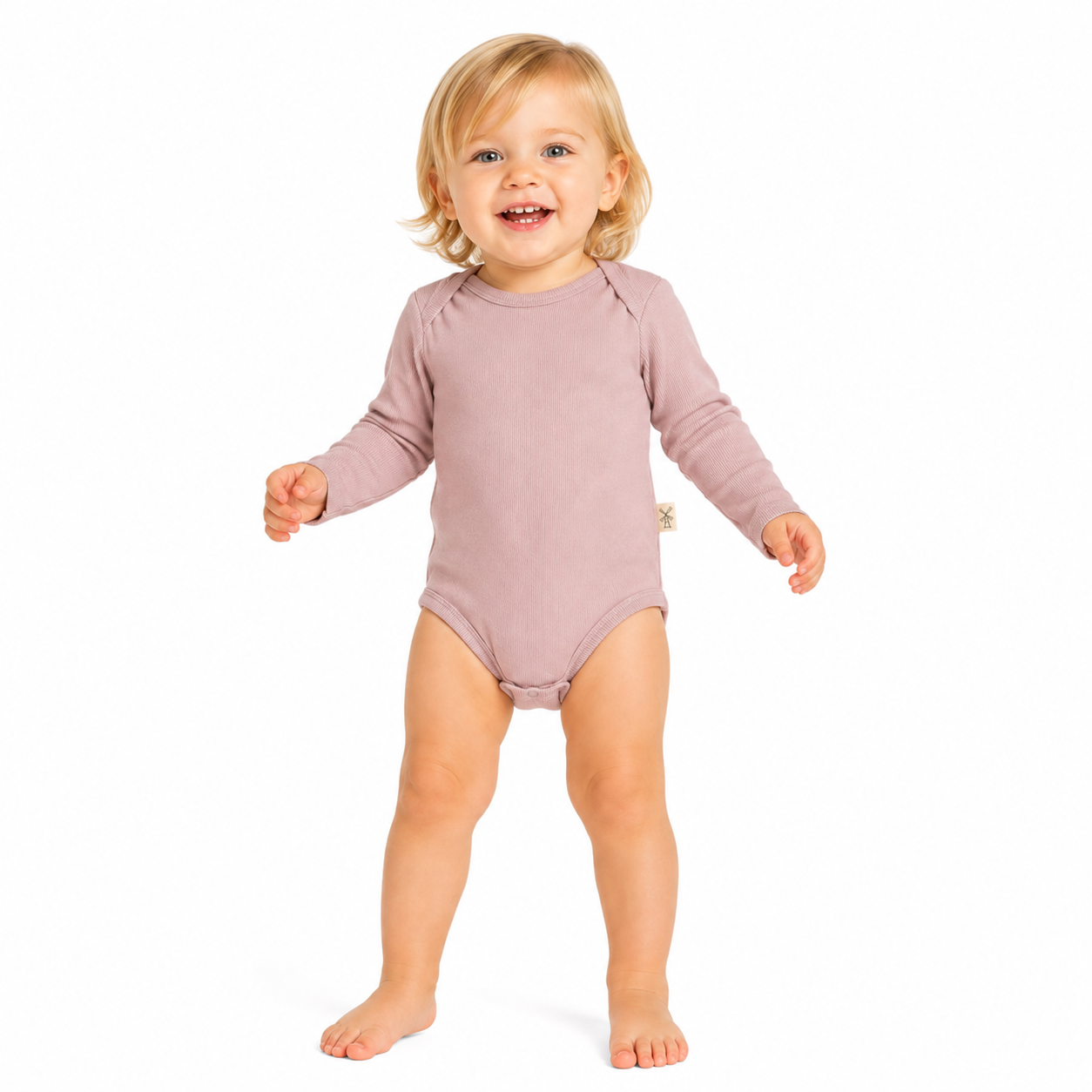 A smiling toddler standing barefoot on a white background, wearing a long-sleeve bodysuit in a muted dusty pink colour.