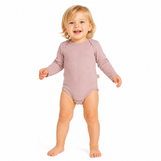 A smiling toddler standing barefoot on a white background, wearing a long-sleeve bodysuit in a muted dusty pink colour.