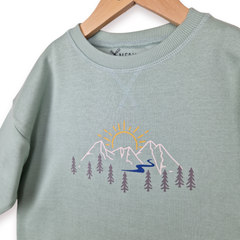 Light green sweatshirt with mountain and sun design on a hanger