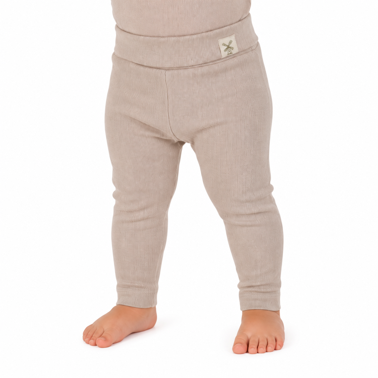 A close-up of a child's lower body wearing ribbed knit leggings in a light oatmeal beige color, standing barefoot against a white background.