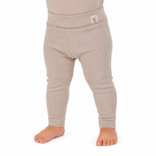 A close-up of a child's lower body wearing ribbed knit leggings in a light oatmeal beige color, standing barefoot against a white background.