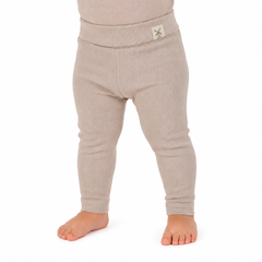 A close-up of a child's lower body wearing ribbed knit leggings in a light oatmeal beige color, standing barefoot against a white background.