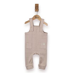 A baby romper in a light beige rib cotton fabric, hanging on a wooden hanger with a wooden peg against a plain white background.