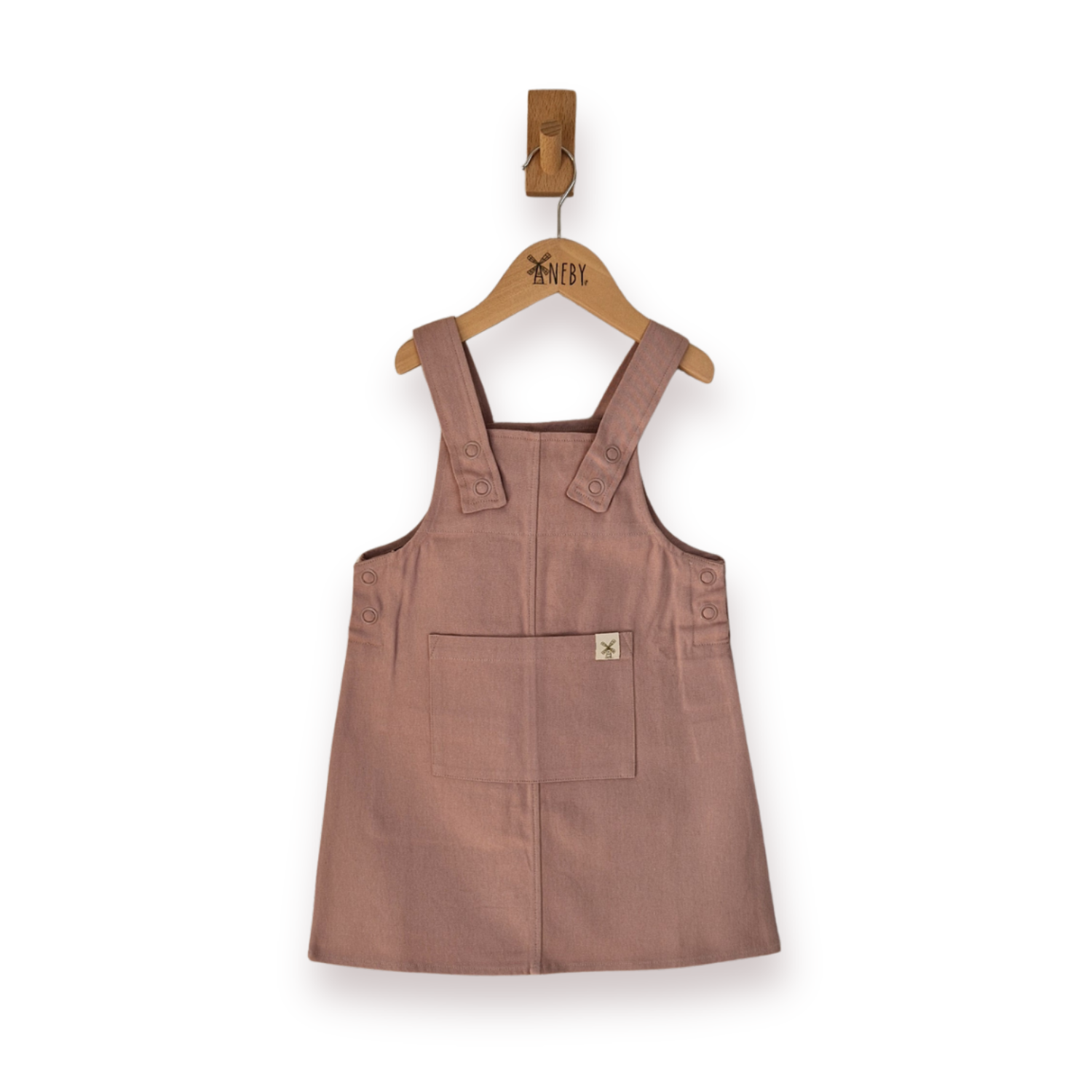 A dusty rose pink pinafore dress for toddlers, hanging on a wooden hanger, set against a plain white background.