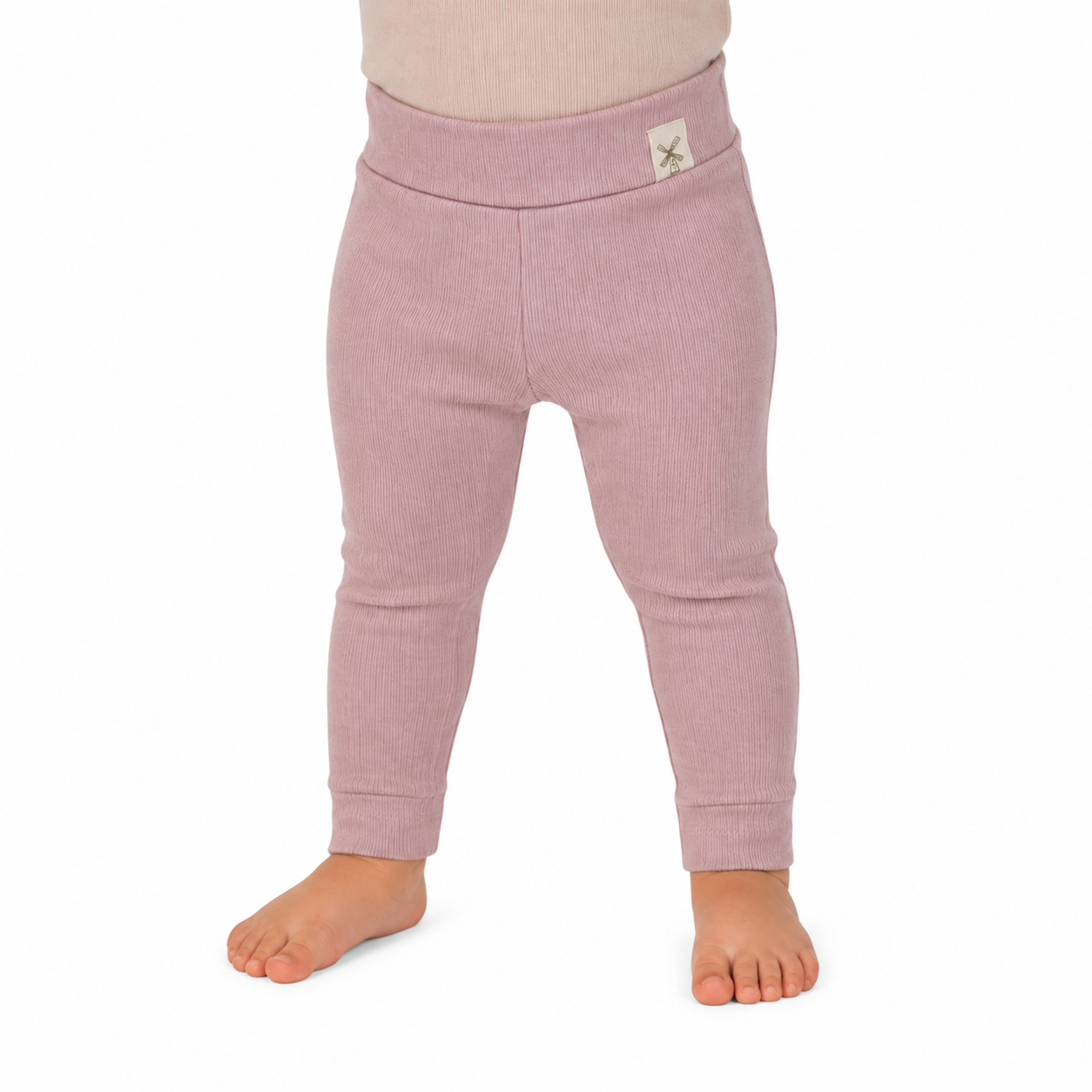 A close-up of a child's lower body wearing ribbed knit leggings in a dusty pink colour, standing barefoot against a plain white background.