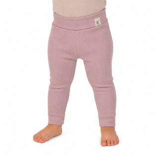 A close-up of a child's lower body wearing ribbed knit leggings in a dusty pink colour, standing barefoot against a plain white background.
