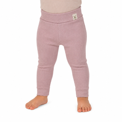 A close-up of a child's lower body wearing ribbed knit leggings in a dusty pink colour, standing barefoot against a plain white background.