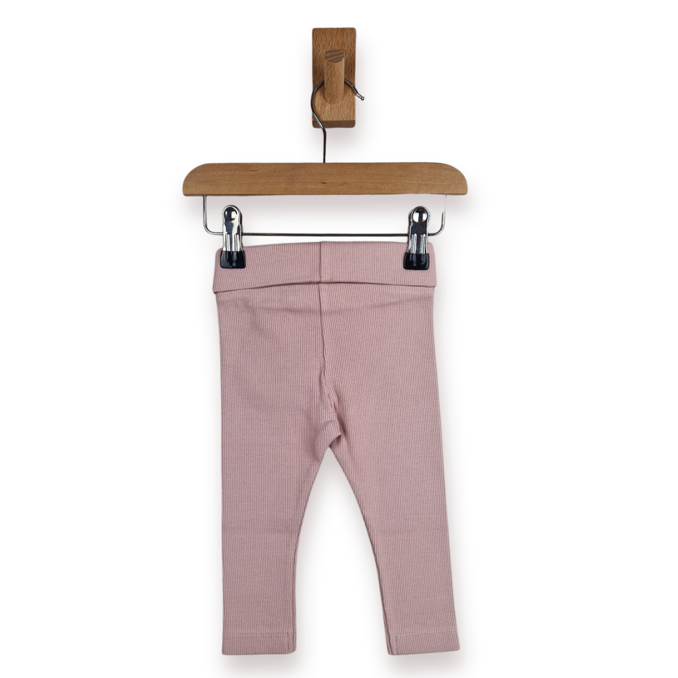 A pair of baby leggings in dusty pink ribbed fabric, hanging from a wooden hanger with metal clips against a plain white background.