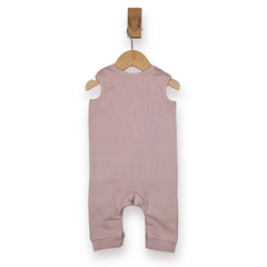 A sleeveless baby romper in dusty mauve pink, hanging on a wooden hanger from a wall hook against a plain white background.