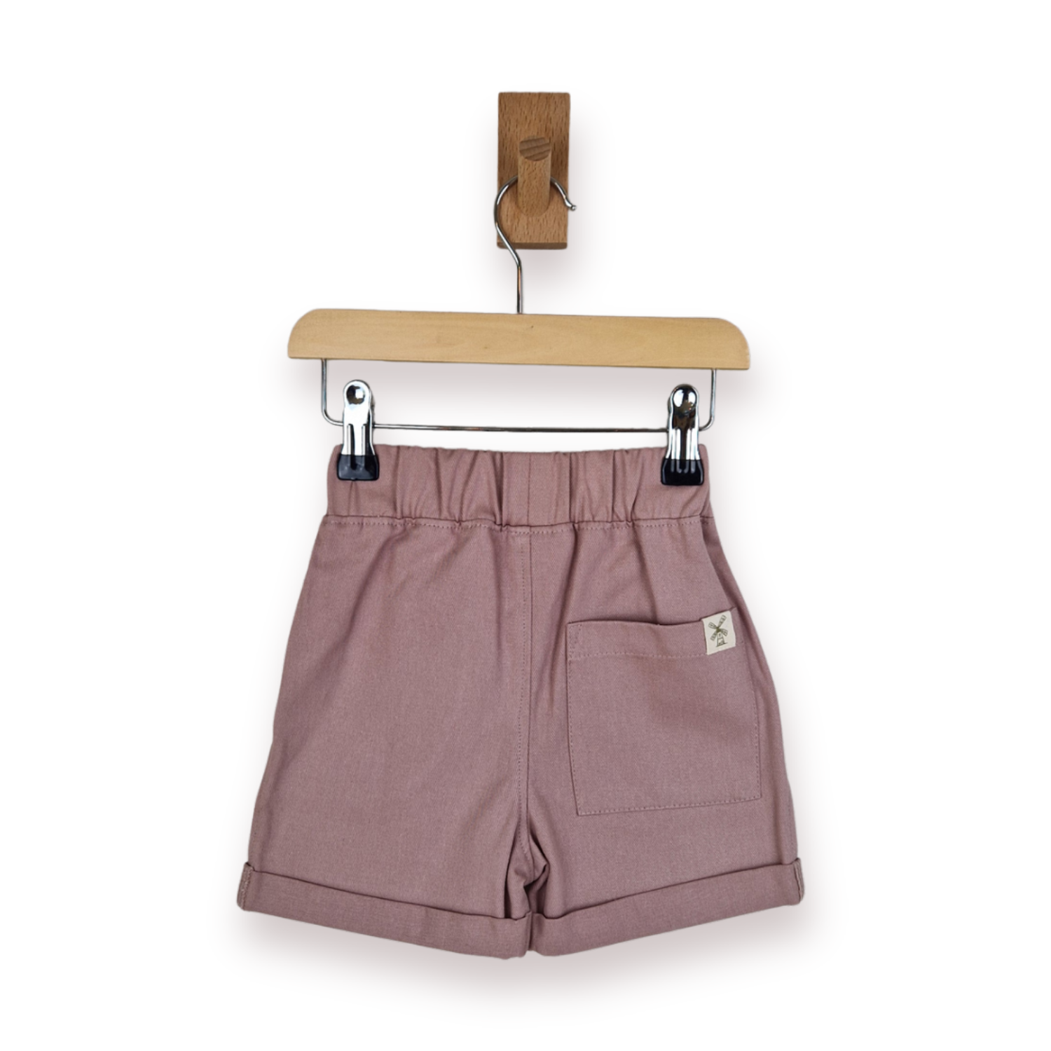 A pair of dusty rose shorts with a gathered elastic waistband, rolled hems, and a side pocket, hanging from a wooden hanger on a white background.