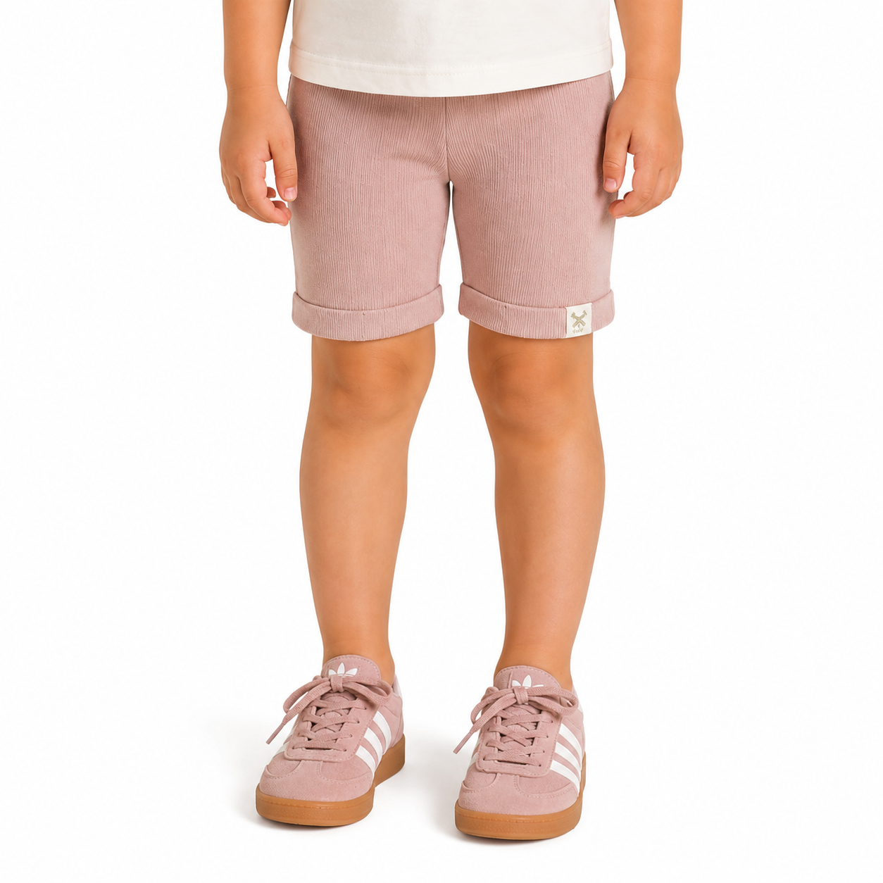 A child wearing dusty pink shorts with rolled cuffs and matching pink trainers, shown from the waist down on a white background.