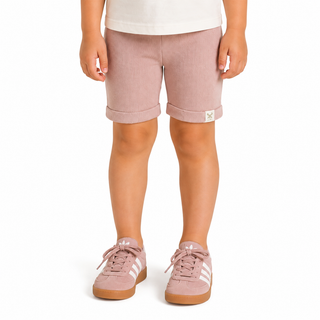 A child wearing dusty pink shorts with rolled cuffs and matching pink trainers, shown from the waist down on a white background.