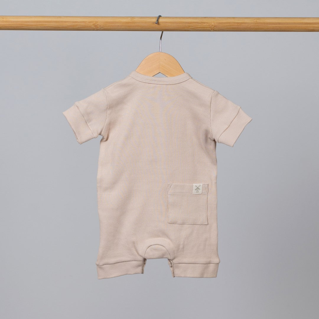 Back view of short sleeve playsuit in beige oat on wooden hanging rail