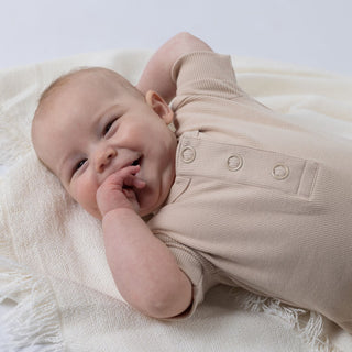 Baby laying down on blanket smiling at the camera wearing beige playsuit